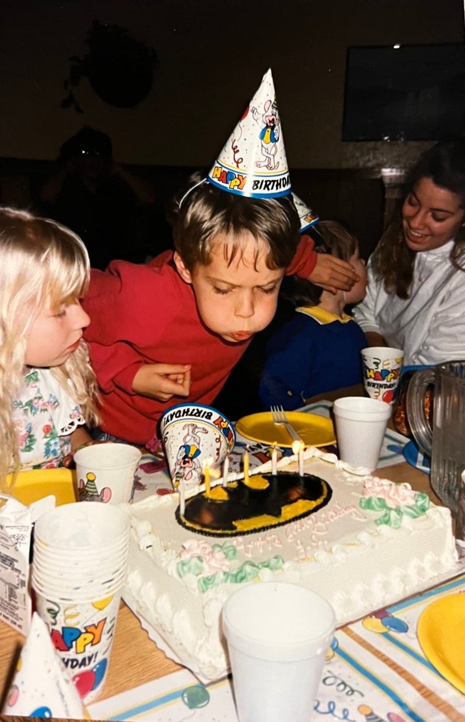 A young Byars brother in a party hat blowing out candles on a Batman birthday cake