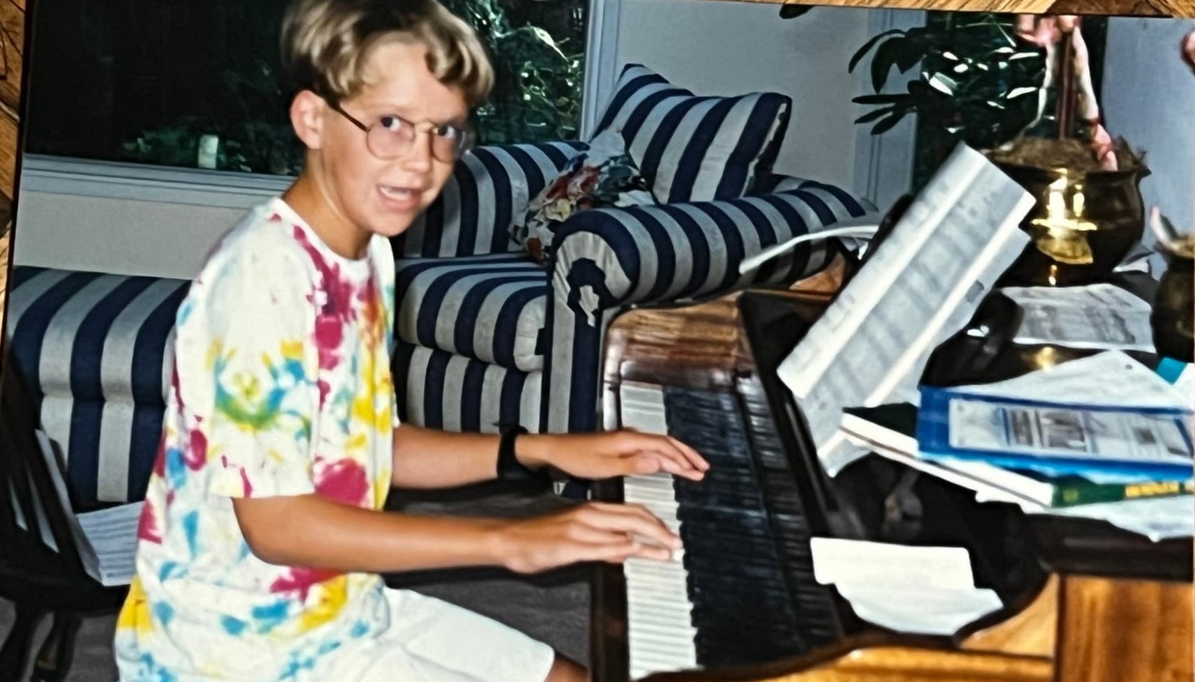 A young Byars brother in a tie-dye shirt playing an upright piano in the living room