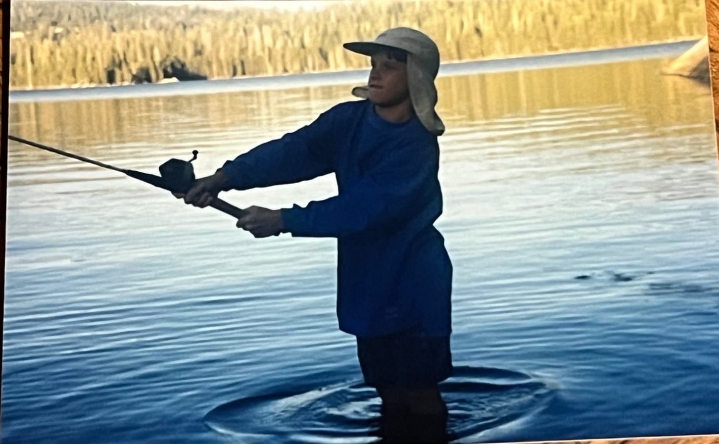 A Byars brother casting a fishing rod into a still lake at golden hour